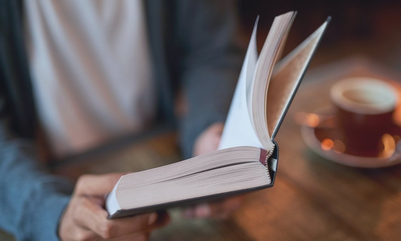 Ahşap masa üzerinde duran kitaplar ve kahve fincanından oluşan edebiyat temalı görsel